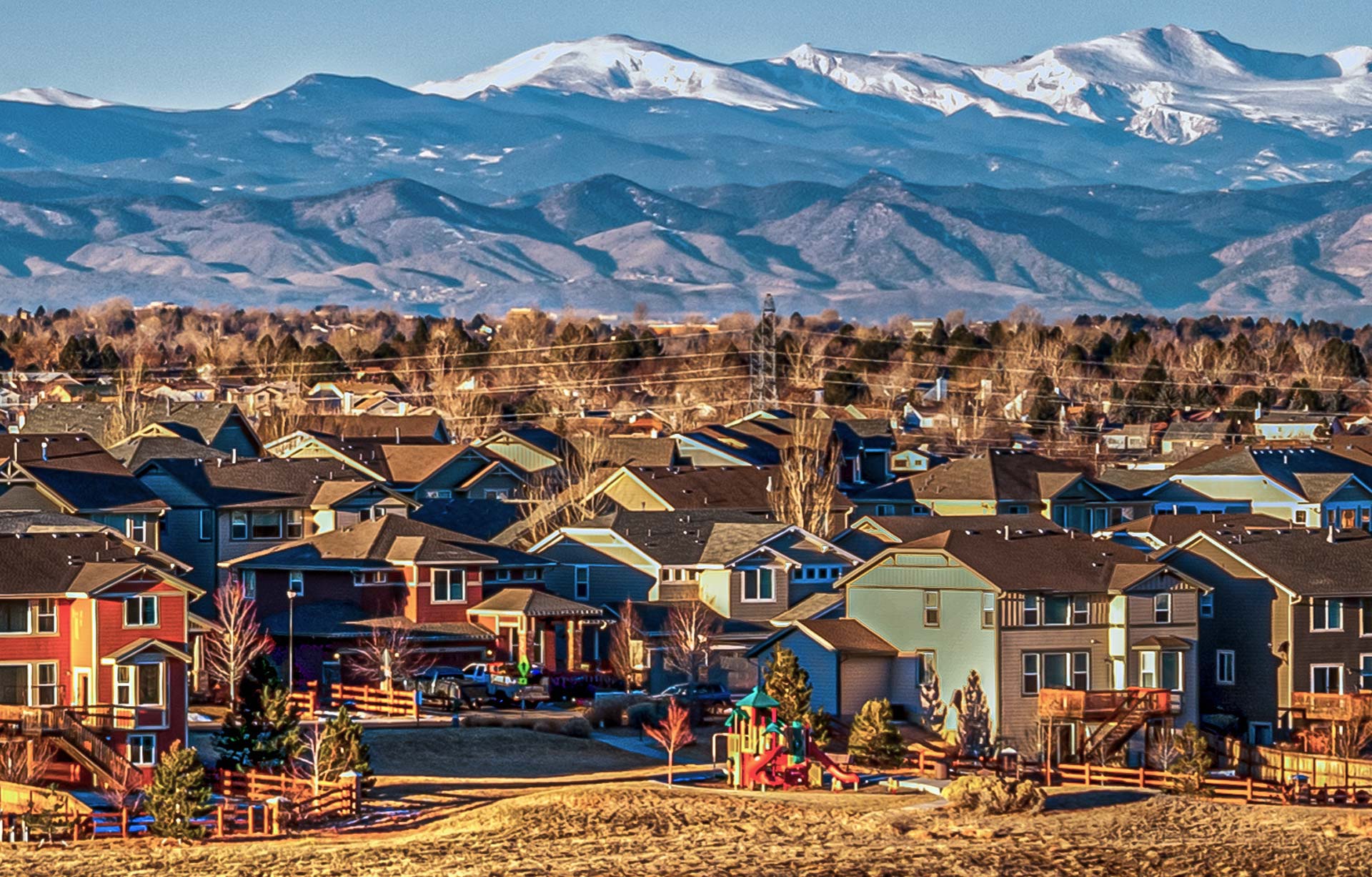Row of homes built along the front range with mountains in the background.