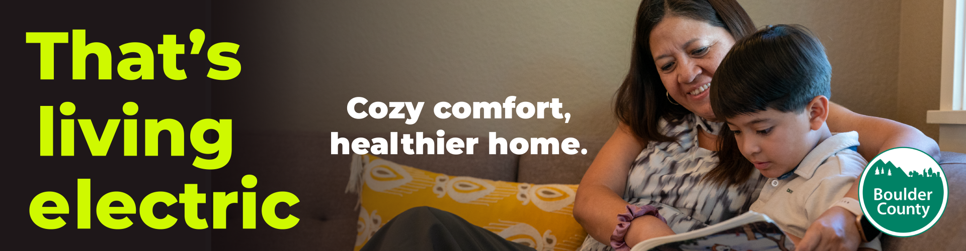 A mother and son cuddle on a couch while reading a book. The image text says, "That's living electric. Cozy comfort, healthier home." There is also a Boulder County logo.