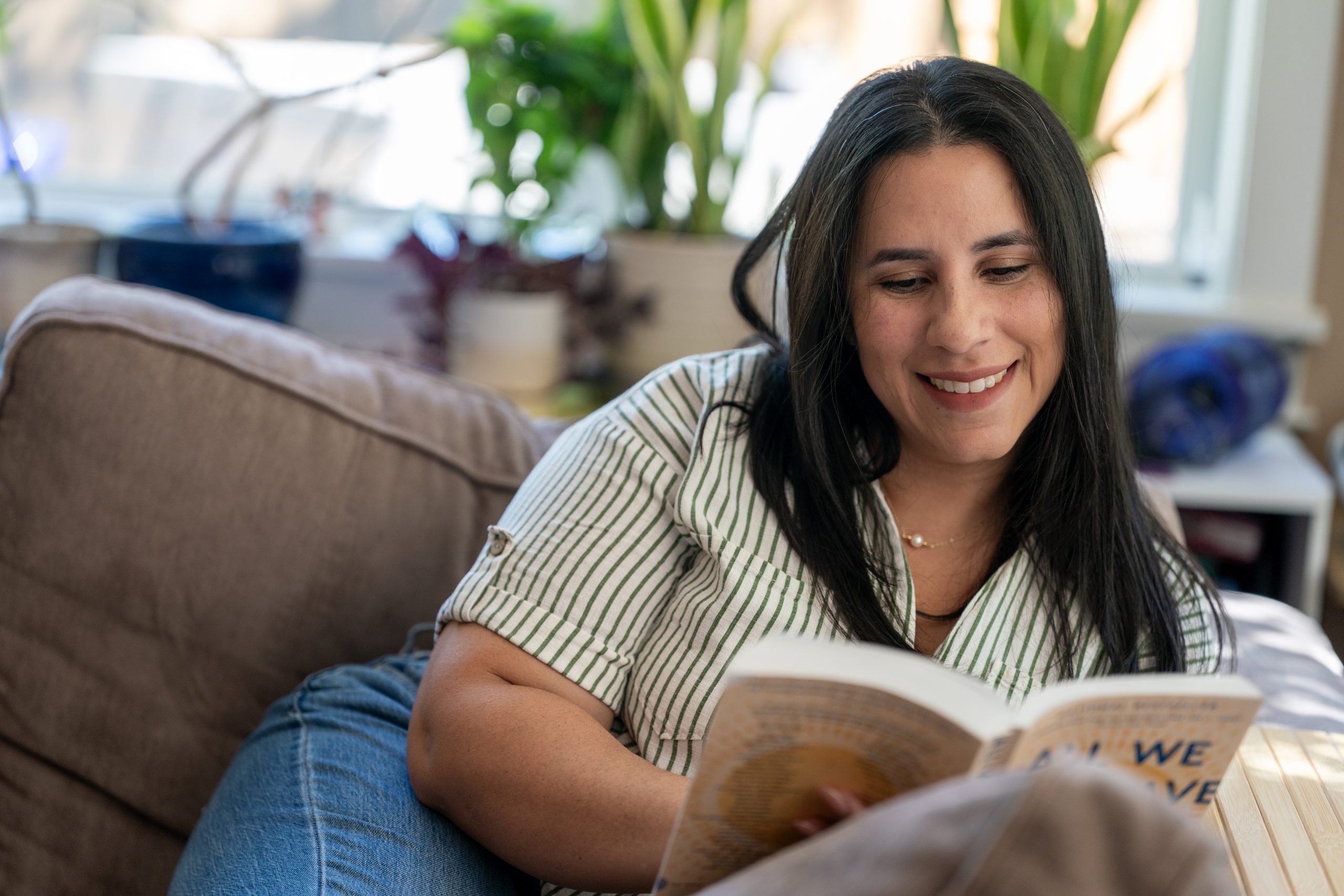 Heat pump Woman reading couch_Living Electric A woman smiles while reading a book on a couch