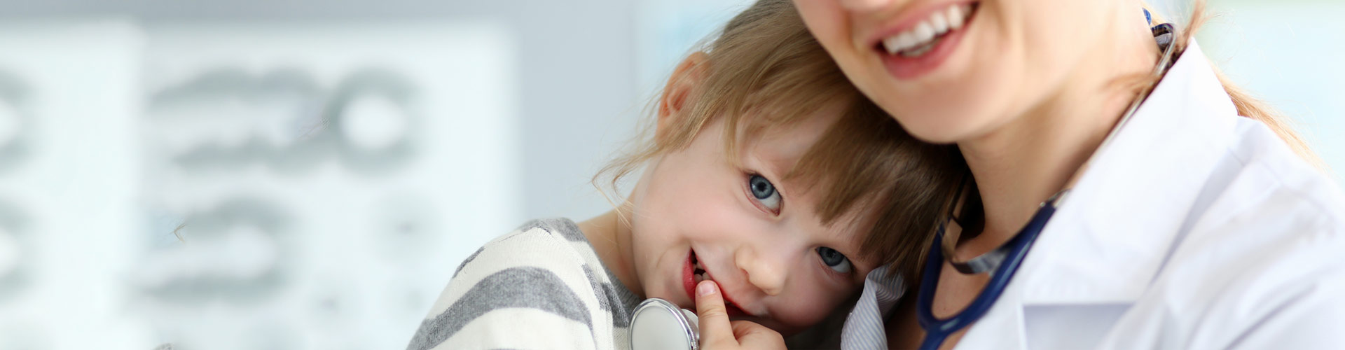 A smiling child rests against a female doctor in a white coat and stethoscope.