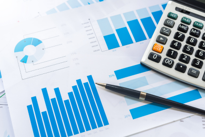 Calculator and pen on top of a paper with charts and graphs.